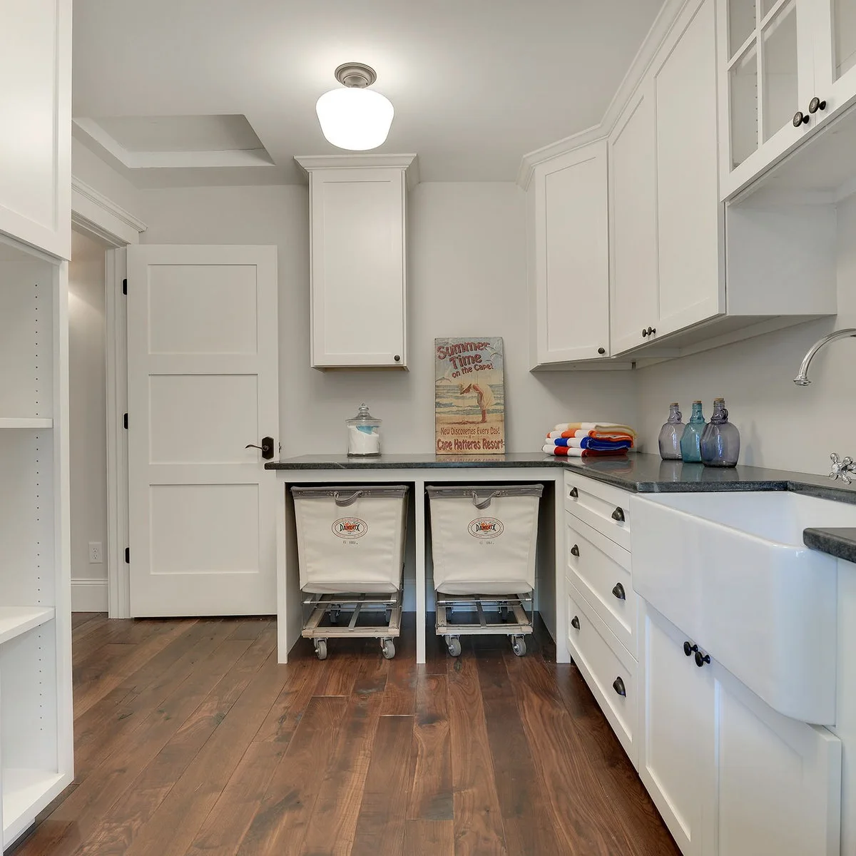 White laundry room with a large utility sink, wraparound counters and two rolling fabric hampers beneath the back counter