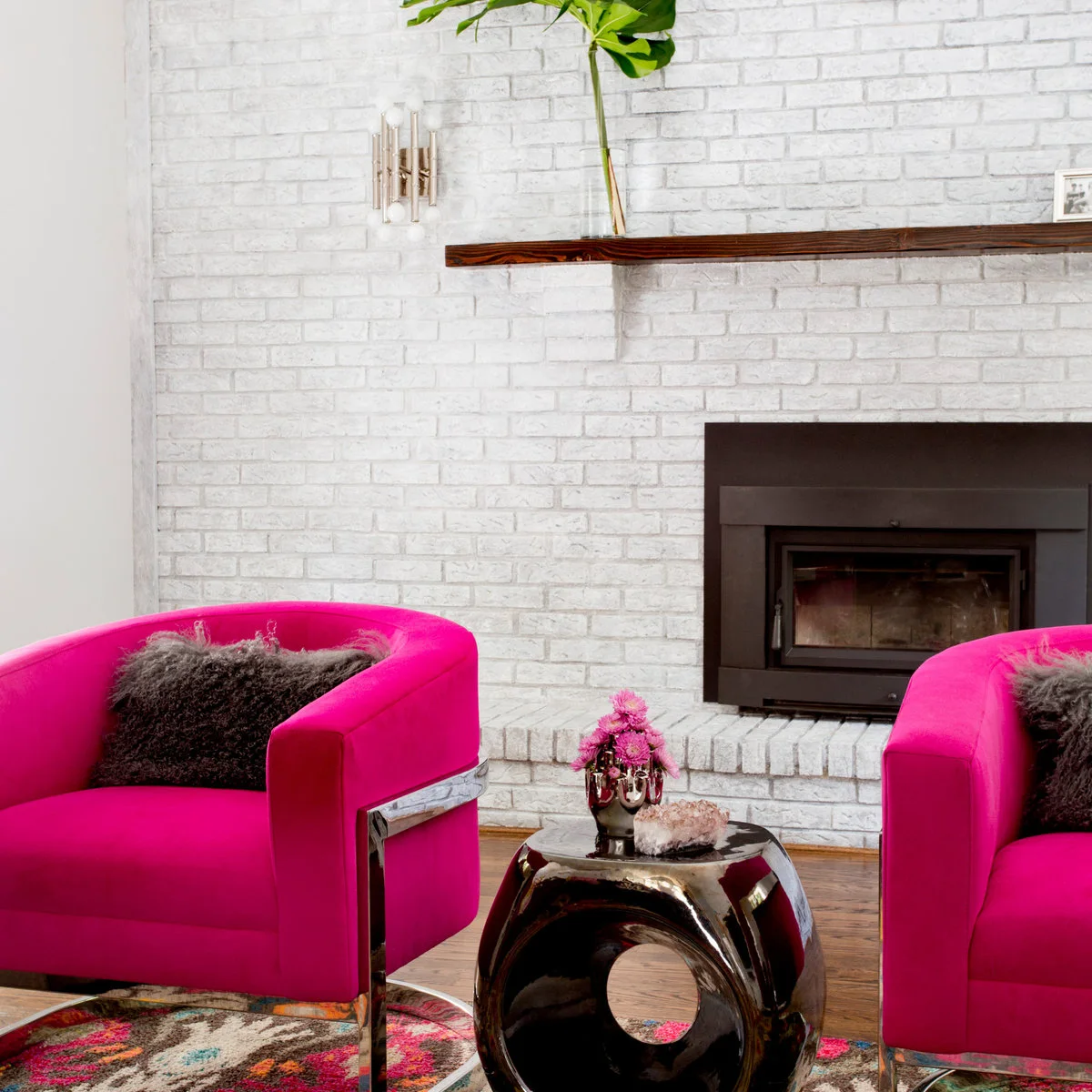 Bright pink chairs with dark charcoal textured cushions beside a white-painted brick fireplace.
