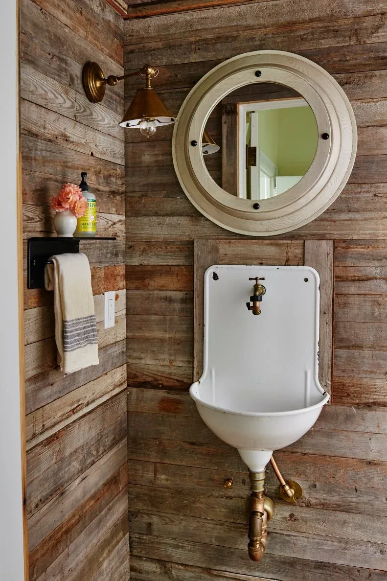 Rustic wood-lined powder room with compact white wall basin, round mirror and warm-toned plumbing