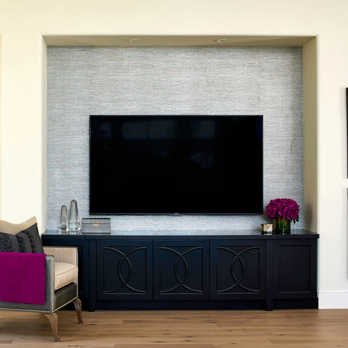 A silver-gray wallpapered TV niche sits above a dark cabinet with curved door details.