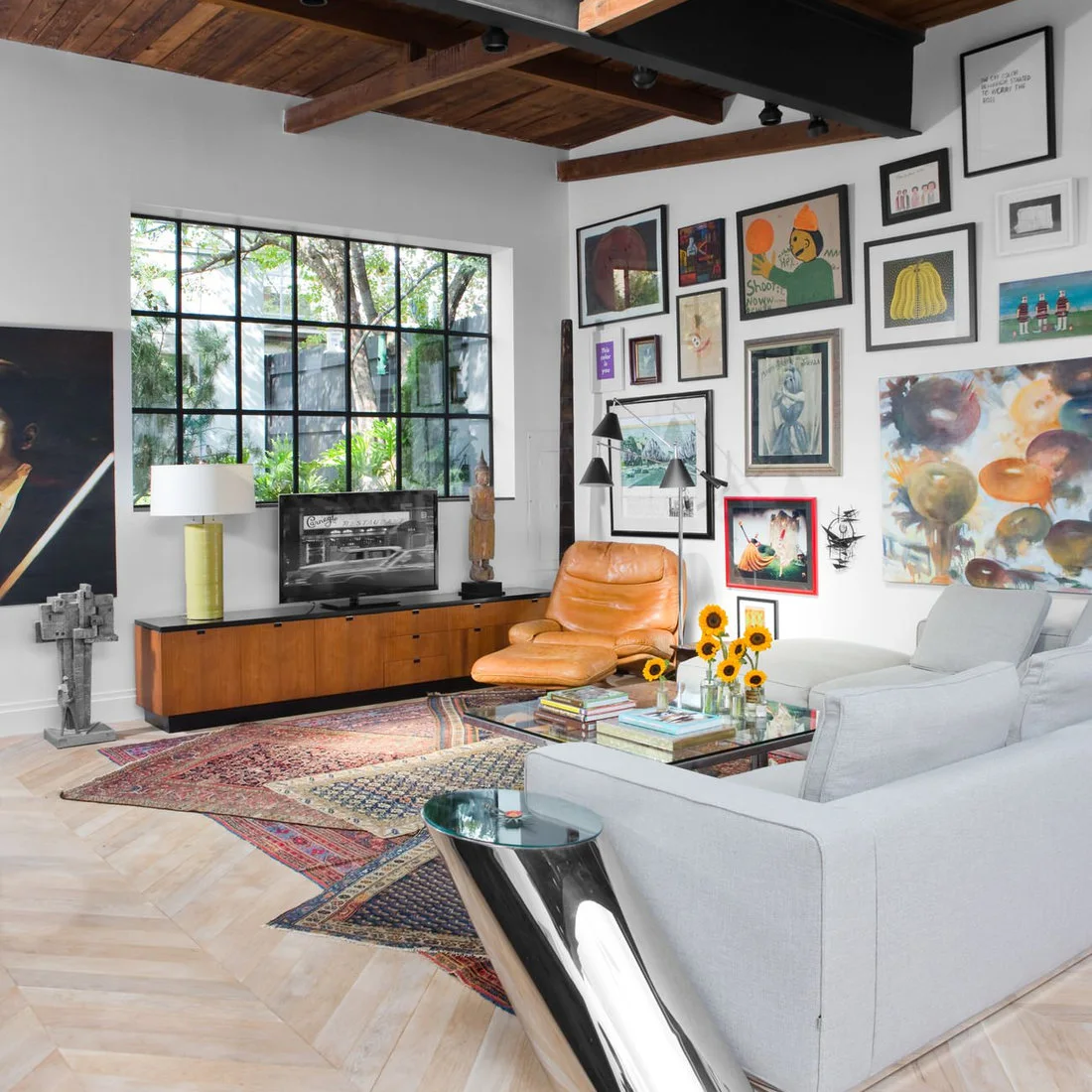 A low wood media cabinet and pale seating beneath timber beams and a colorful gallery wall