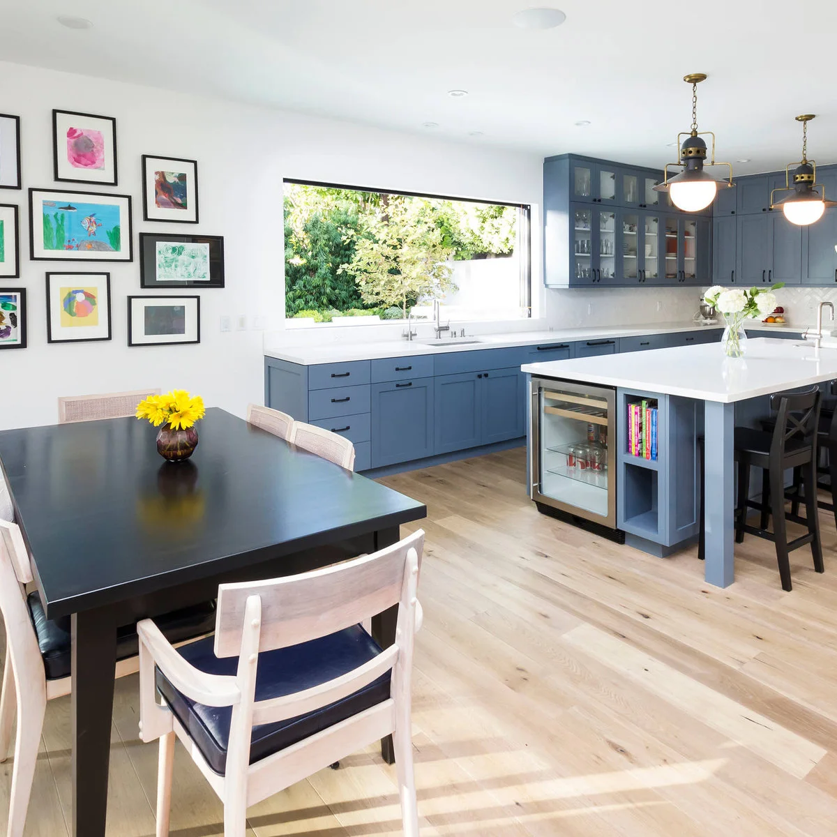 Black-framed colorful drawings beside a dining table in a blue and white kitchen with an island.