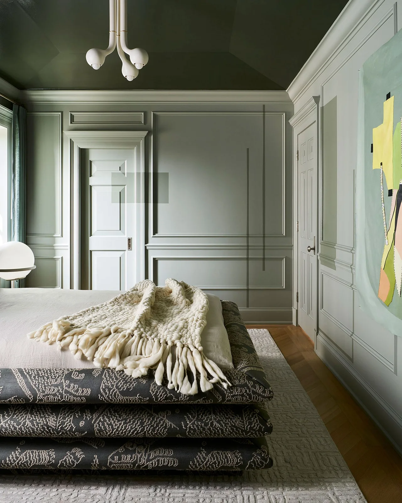 Sage wall moldings and doors frame a bedroom with a darker green ceiling and a patterned upholstered bed.