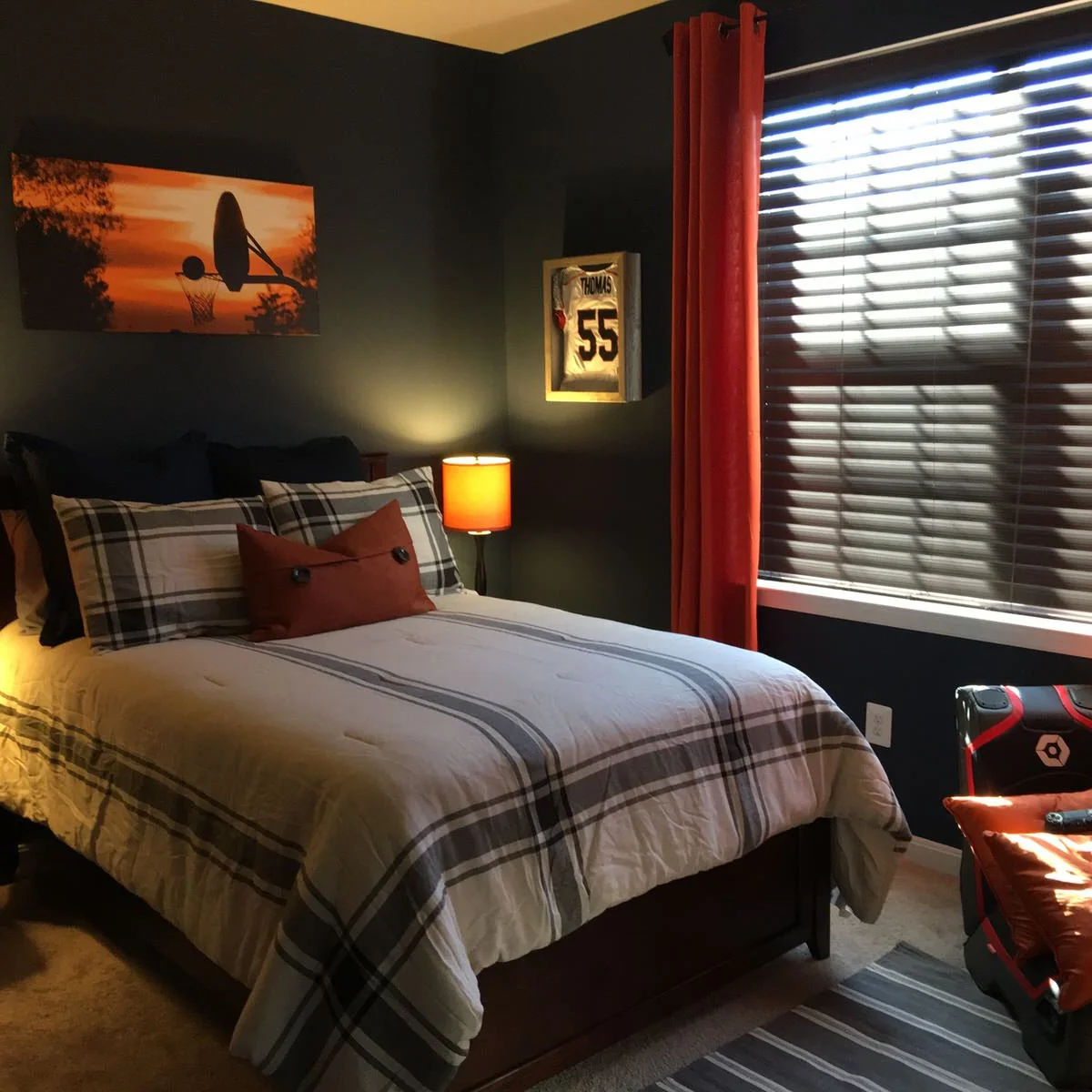 Teen bedroom with dark walls, orange curtains, checked bedding and framed basketball imagery