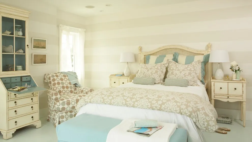 A pale bed sits beside vintage-style cabinets, patterned chairs, and soft blue-green bedding