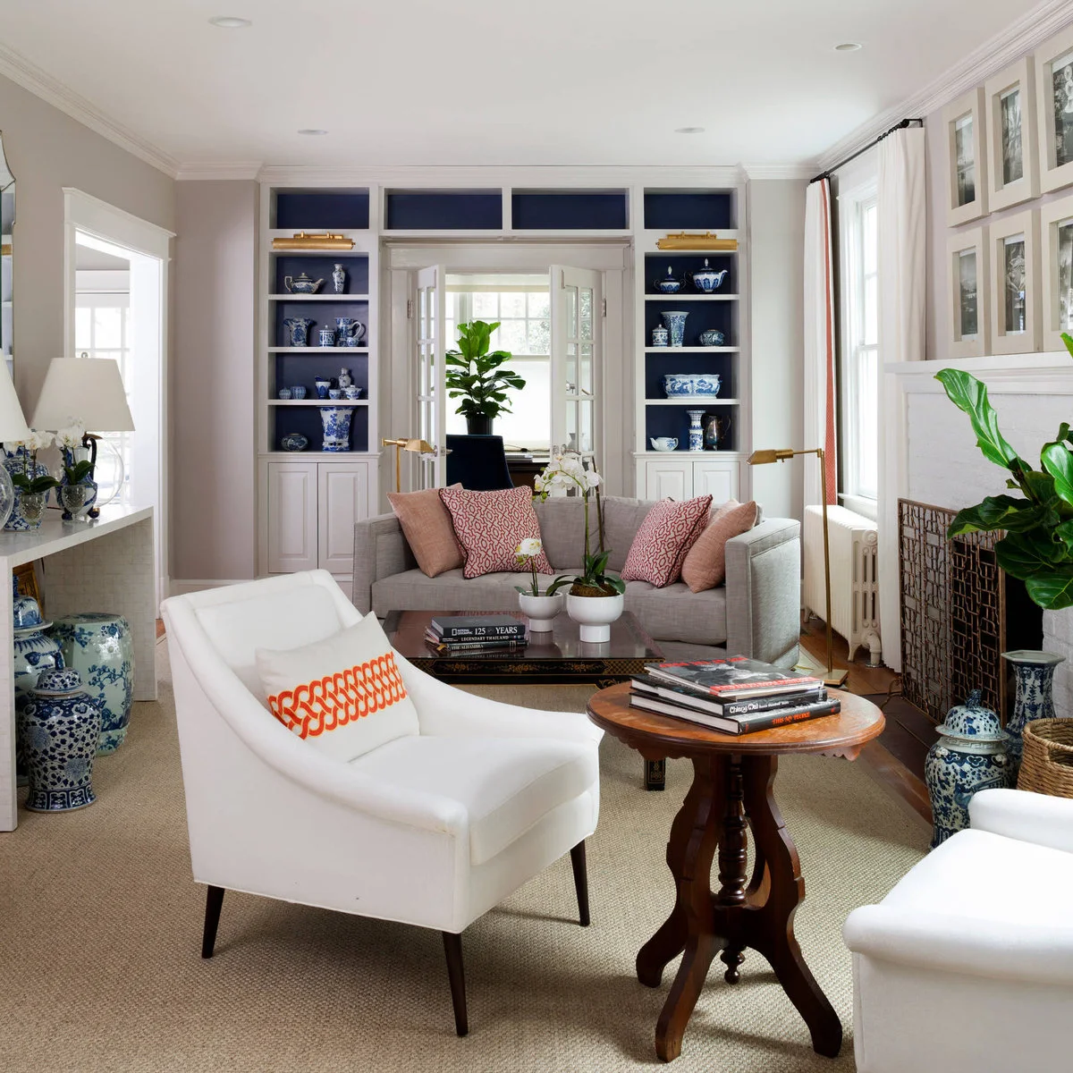 Narrow traditional living room with navy-backed shelves around a doorway, gray sofa and white armchairs