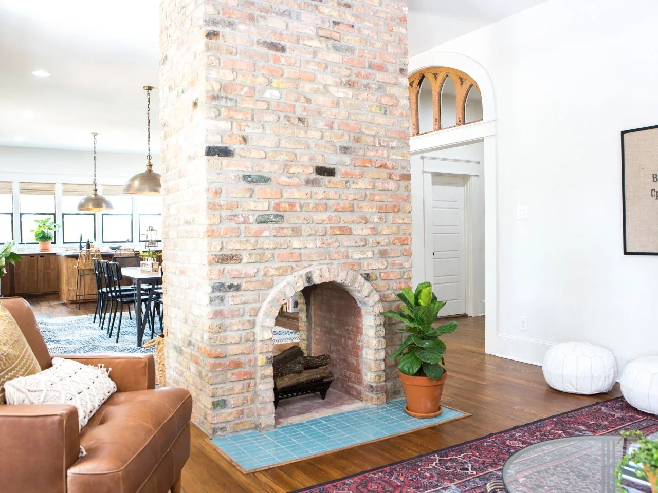 An arched exposed-brick fireplace divides shared rooms above a blue-tiled hearth beside a tan sofa.