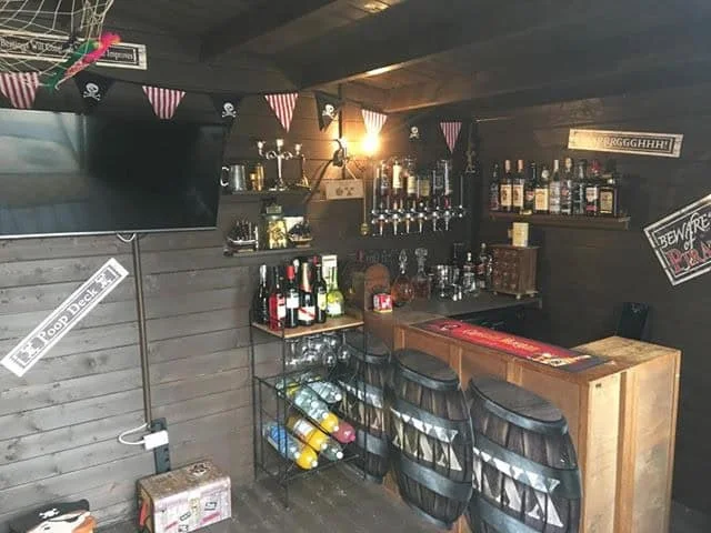 Dark timber shed interior with a small corner bar, bottle shelves and decorative barrel shapes