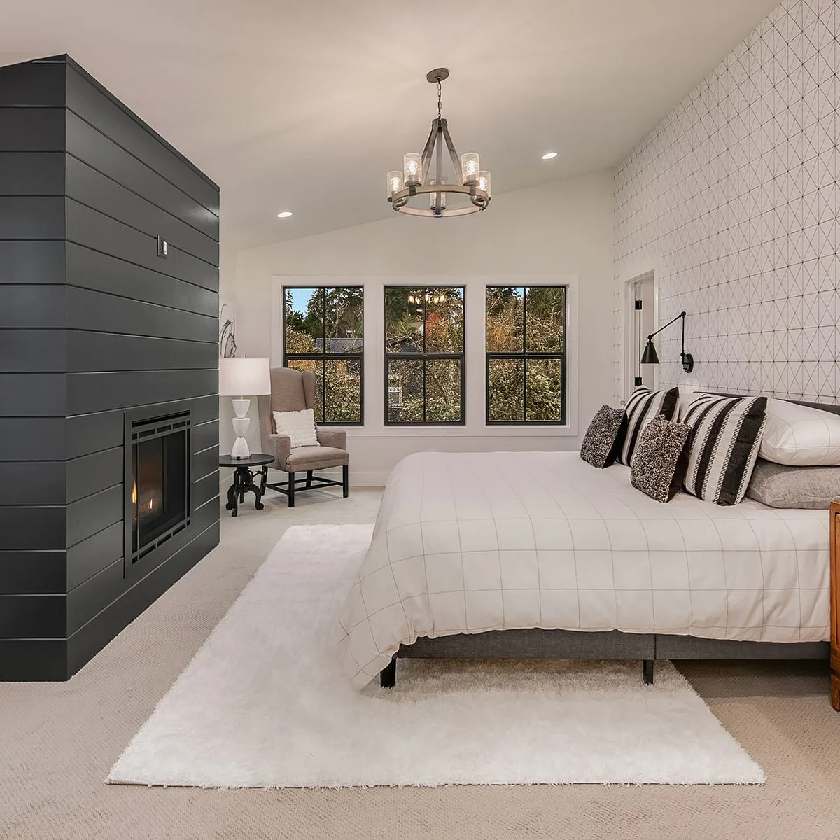 Charcoal board-clad fireplace wall opposite a bed with fine geometric wallpaper behind it