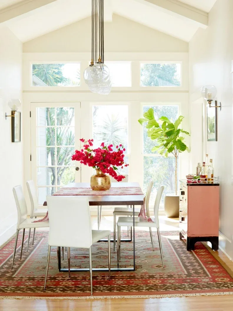 Coral dining sideboard viewed from its end beside a wood table, white chairs and a red patterned rug