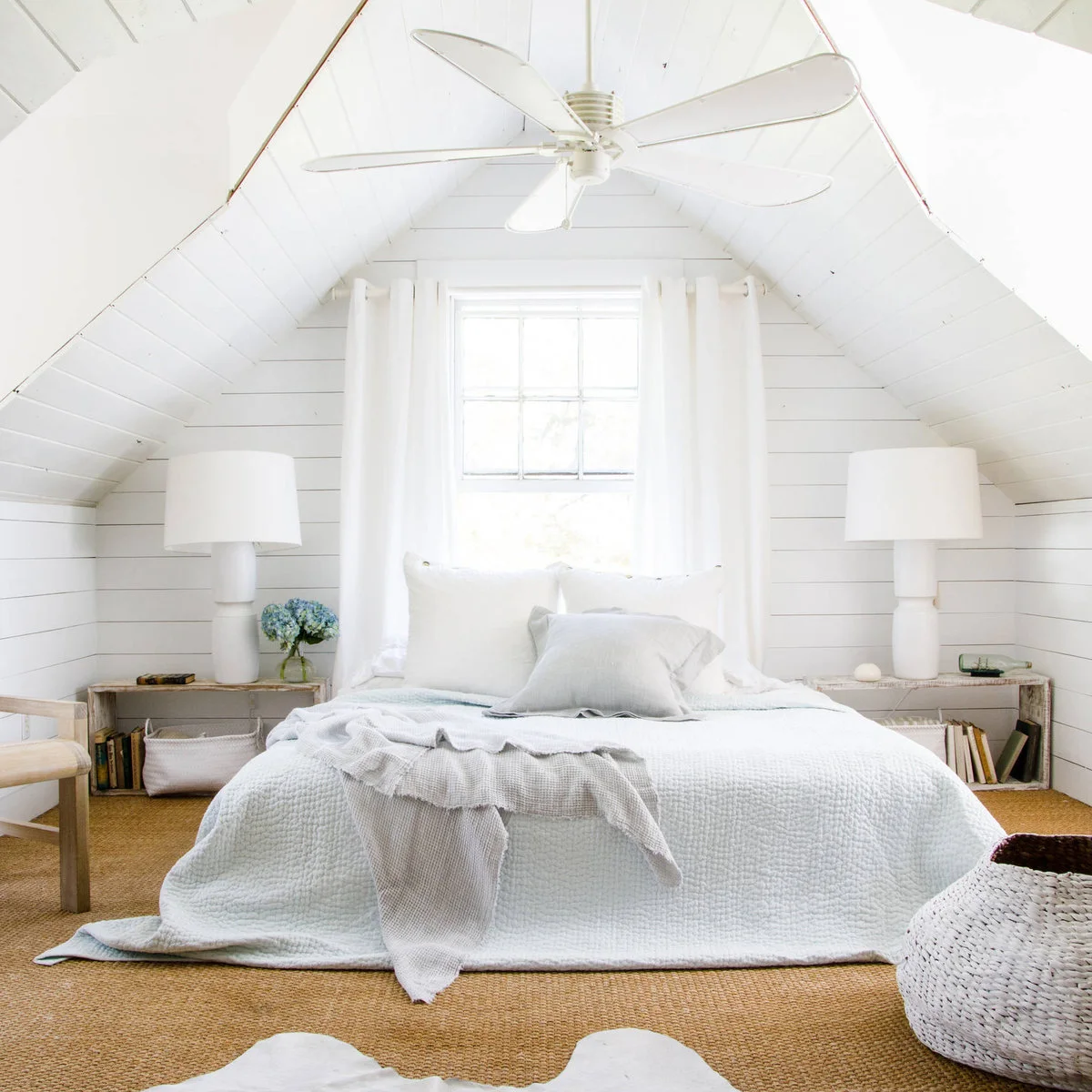 White attic bedroom with pale textured bedding, matching lamps and low open bedside storage