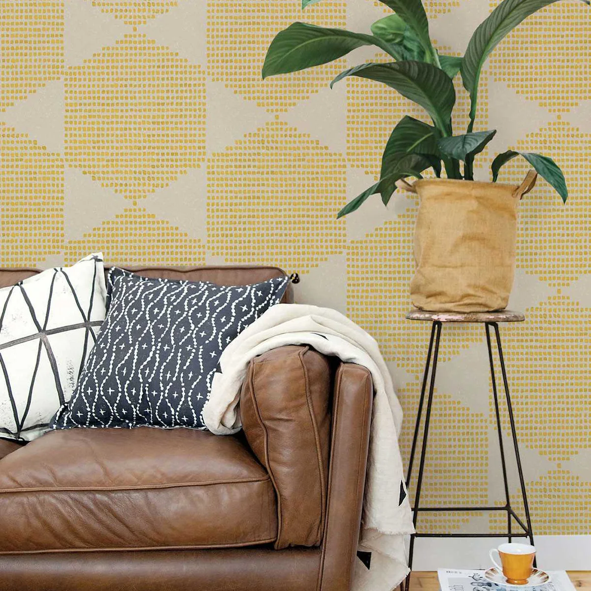 Brown sofa corner with black-and-white cushions against a yellow dotted wall pattern and a tall plant stand