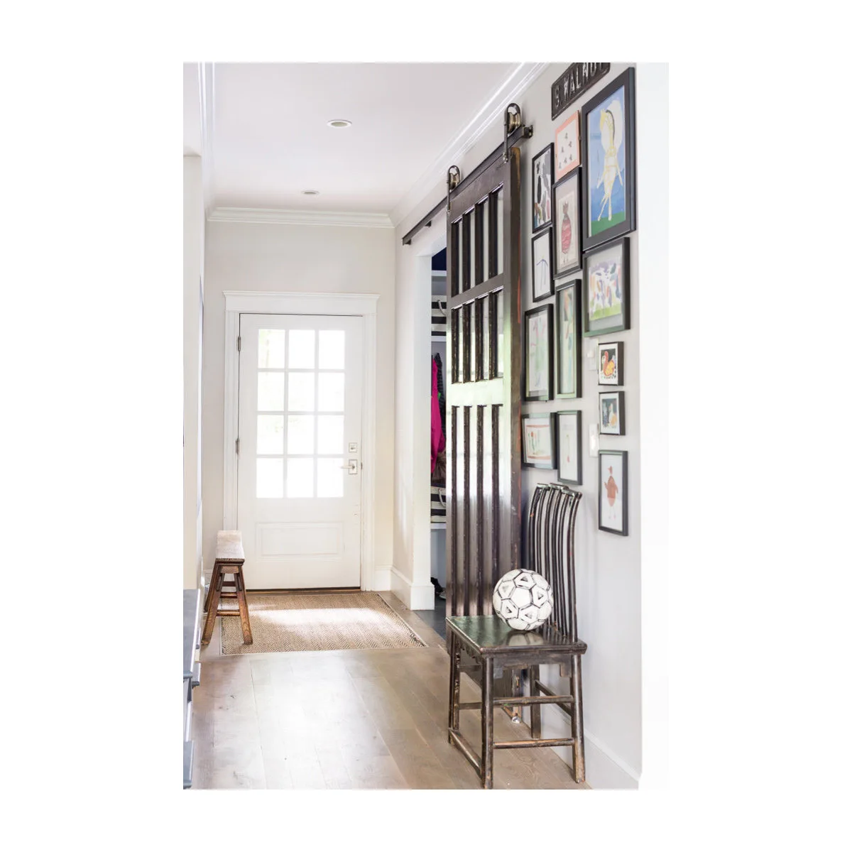Narrow entrance with a white glazed door, dark sliding door, a wooden chair and a cluster of framed pictures.