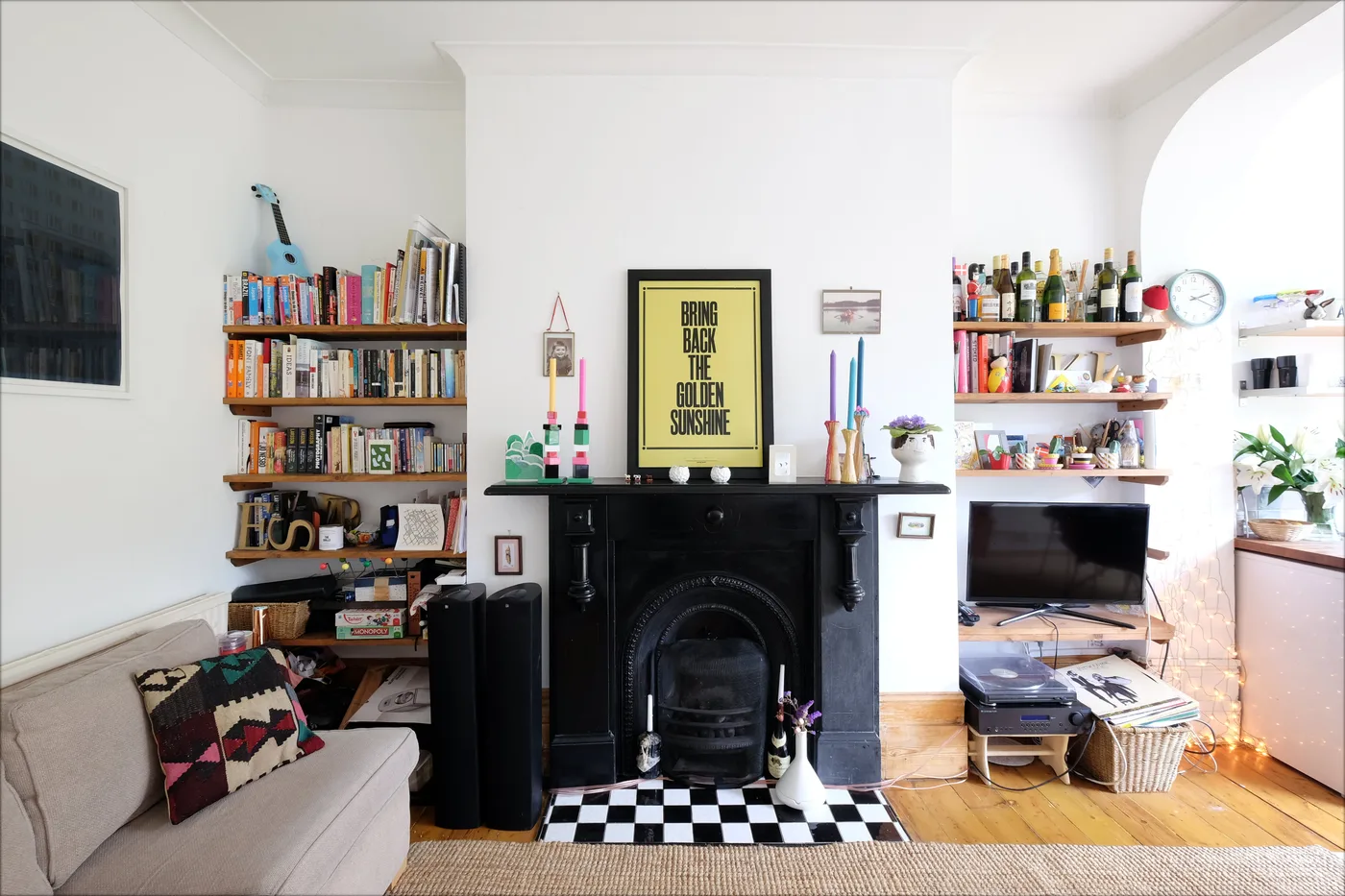 Black fireplace beneath colorful tapers in bottle-shaped holders, surrounded by books and a black-and-white hearth.