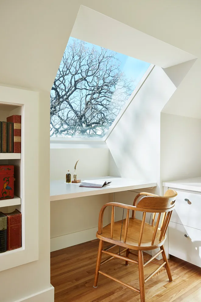 A small pale desk sits beneath a roof window beside a timber chair