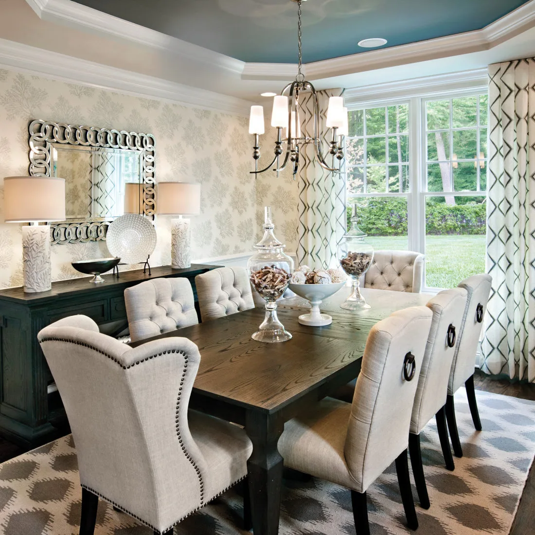 Gray and white patterned rug beneath cream dining chairs and a wood table beside geometric curtains