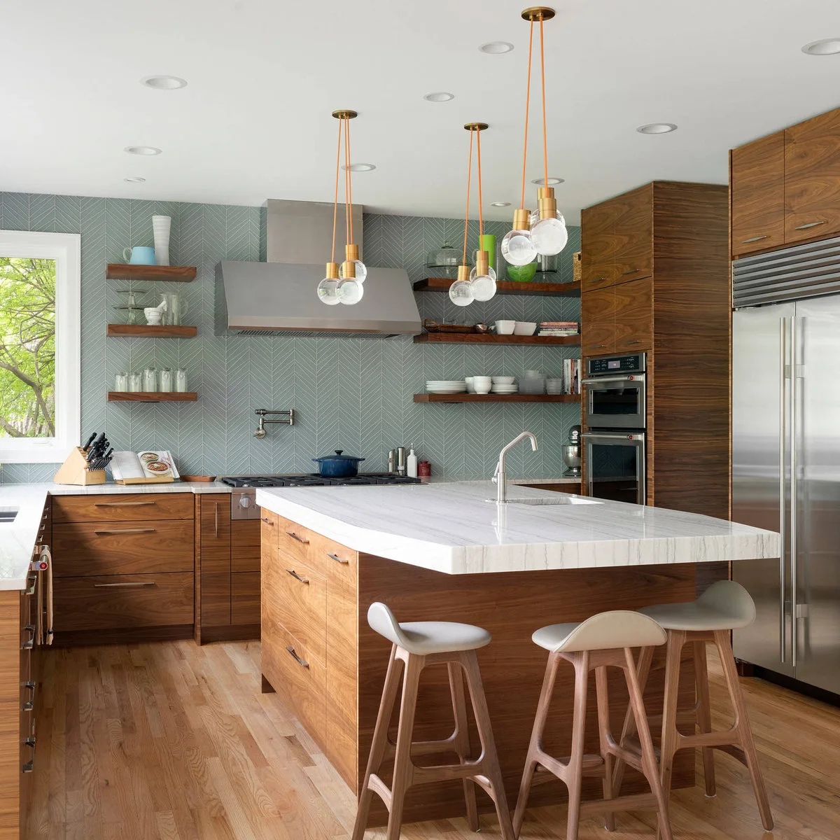 Wood cabinets and a pale island beneath groups of glass globe pendants with orange cords and warm metal fittings.
