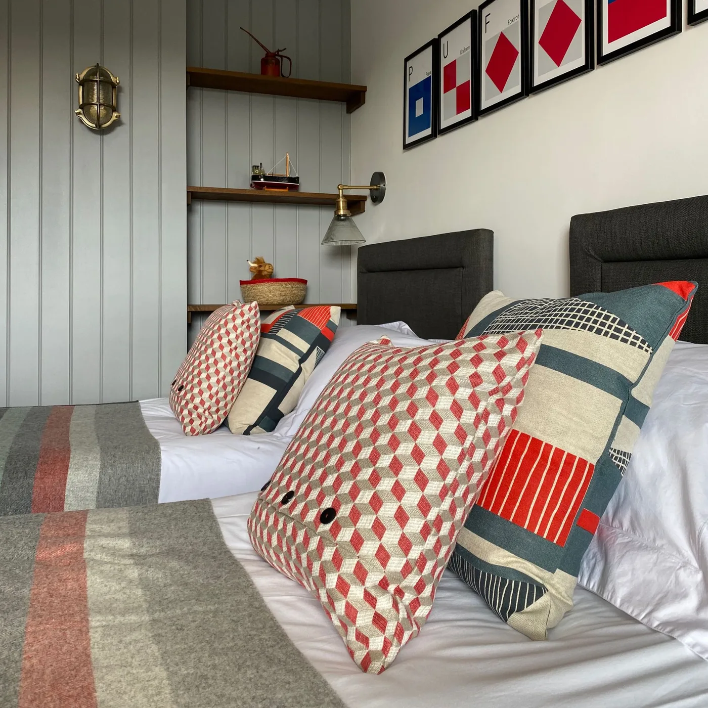 Shared bedroom with dark twin headboards, gray wall paneling, nautical flag pictures and red-and-blue patterned cushions.