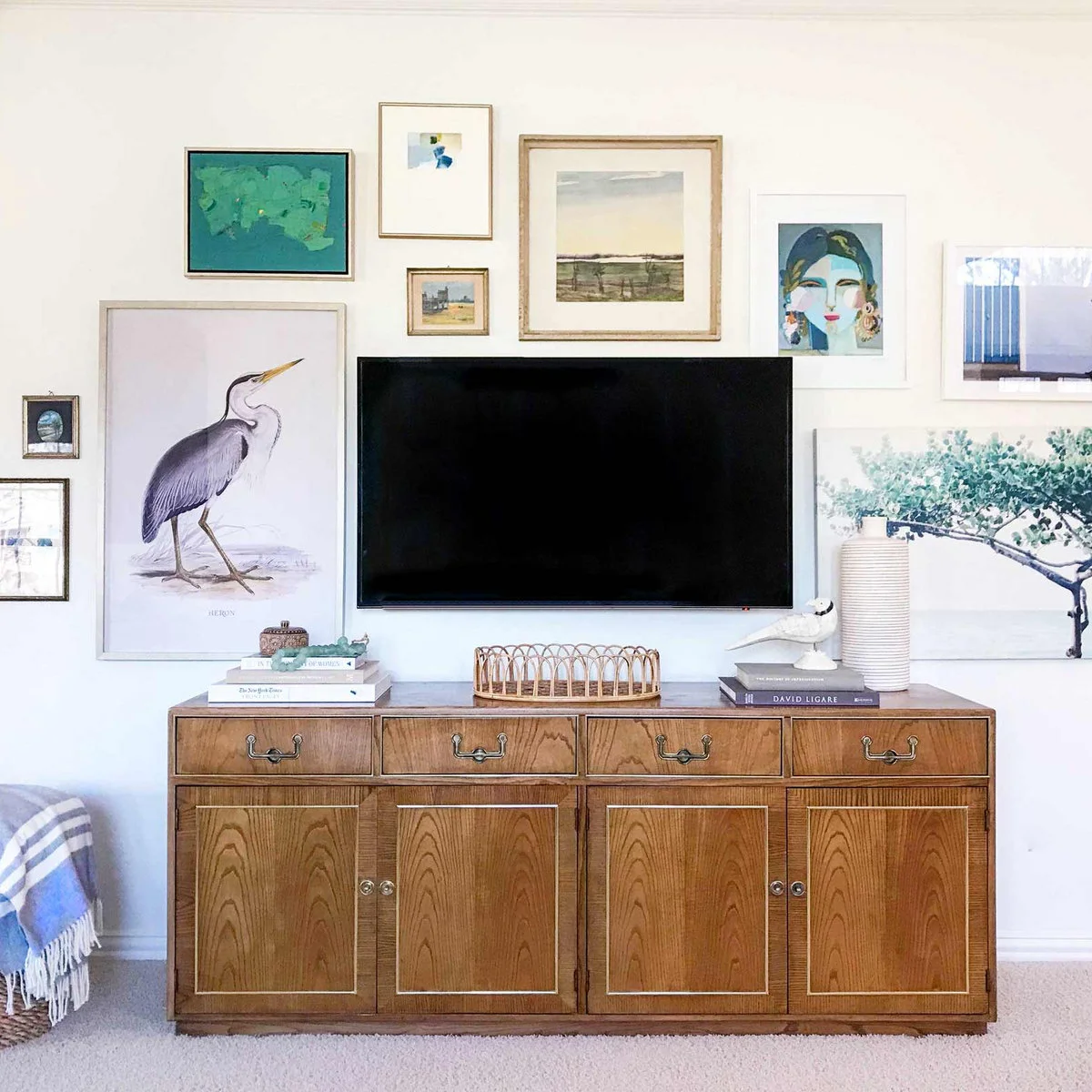 Bird, landscape, tree and portrait pictures above and beside a television over a traditional wood cabinet.