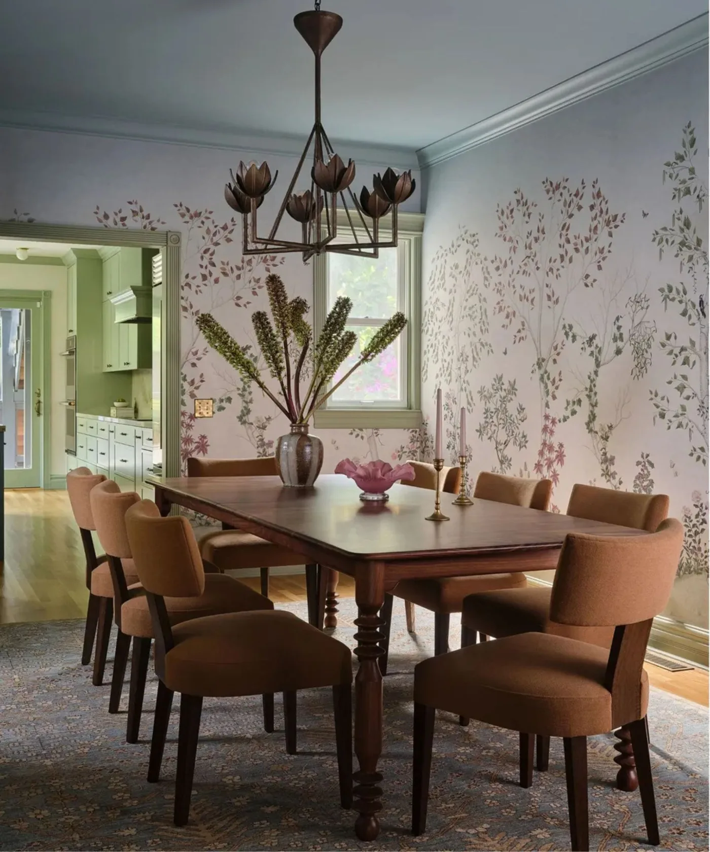 Pale floral dining room with a turned-leg wooden table, warm brown upholstered chairs and a flower-shaped chandelier.