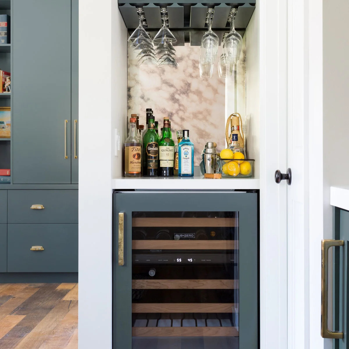 Slim mini bar niche with hanging wine glasses, bottles, cocktail shaker and wine refrigerator beneath
