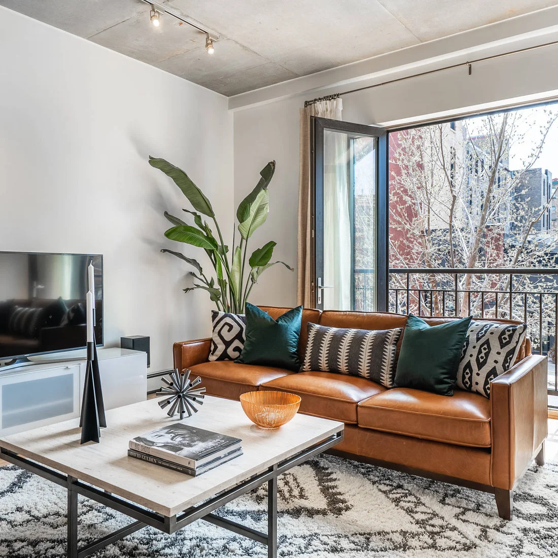 A brown sofa with graphic cushions beneath a concrete ceiling beside an open balcony door