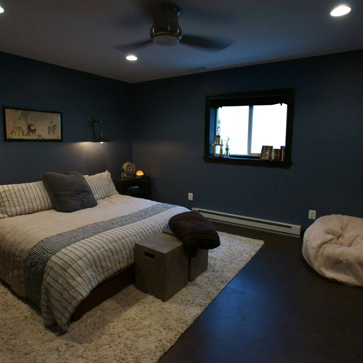 Dark blue teen bedroom with a low bed, pale rug, beanbag seat and wall-mounted reading light
