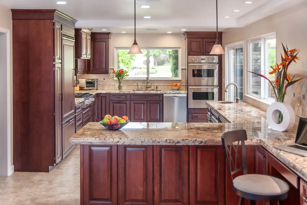 Deep reddish wood cabinets surround a bright kitchen with patterned stone counters