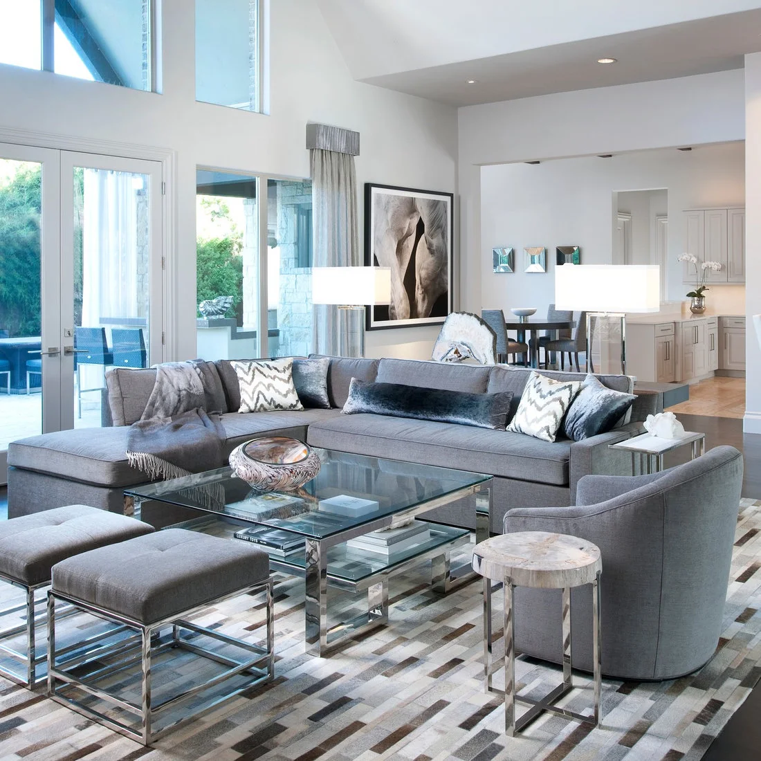 Two rectangular white lamp shades rise behind a gray sectional that separates a living room from a dining area.