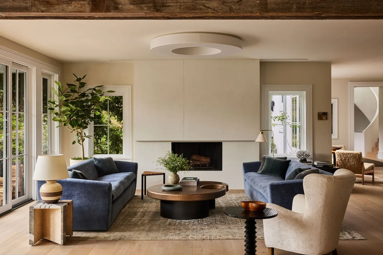 Two blue sofas gather around a low round table beneath pale walls and a timber beam.