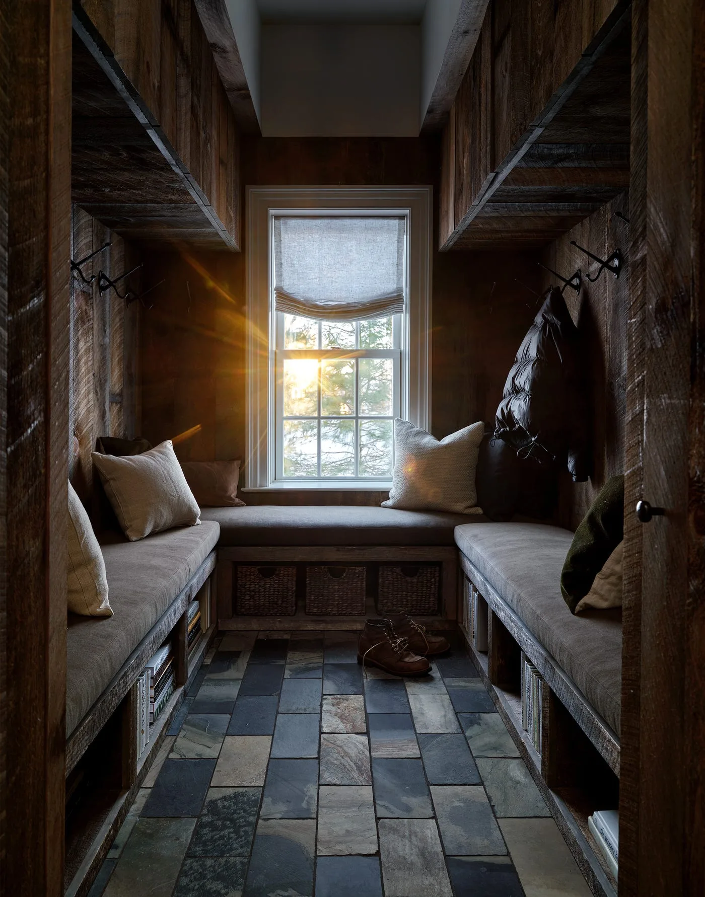 Dark timber-lined entry storage with U-shaped padded bench, lower woven baskets, high open shelves, coat hooks and mixed-tone floor