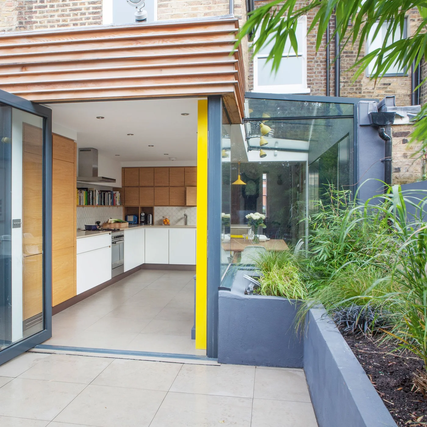 An open kitchen doorway leads to pale courtyard paving beside a raised gray planting bed