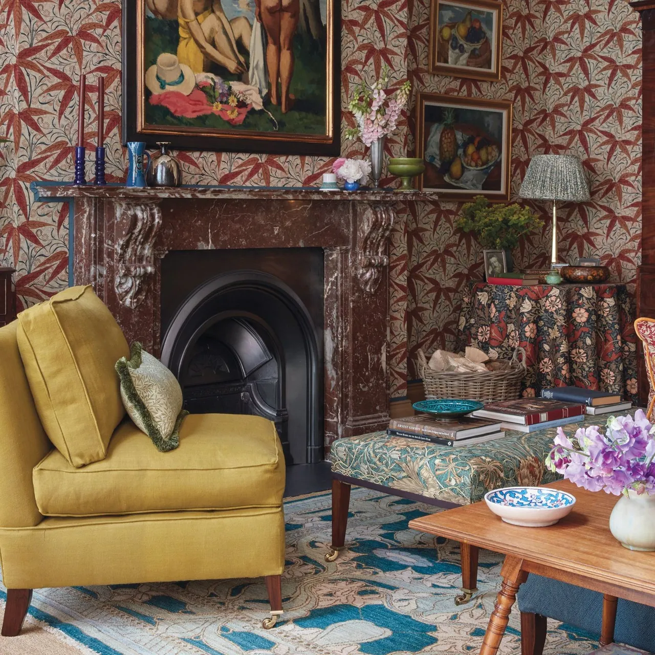 Dark veined fireplace mantel with reddish tapers in blue holders beneath colorful artwork and patterned wallpaper.