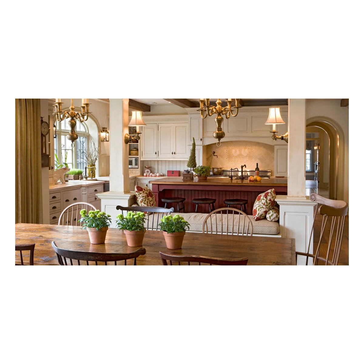 A cushioned bench sits between white posts behind a wood dining table, with a red kitchen island beyond.