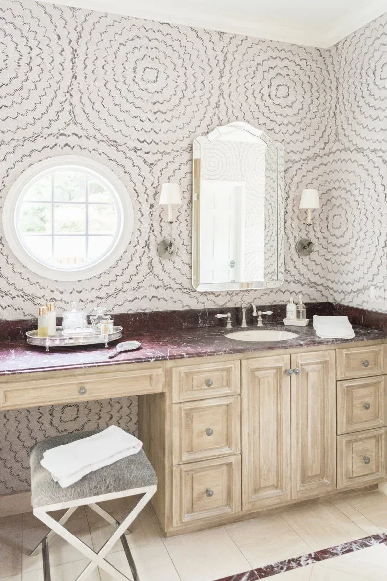 Pale wood bathroom vanity beneath soft circular wall pattern with a warm purple-toned counter