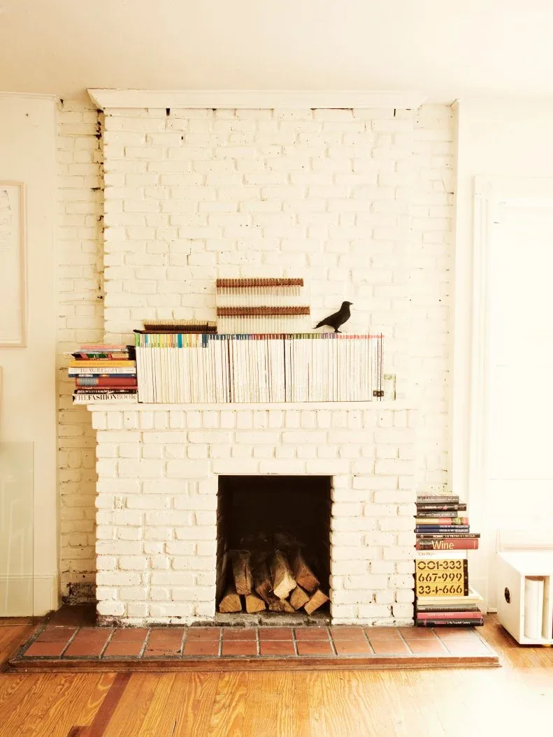 White-coated brick fireplace with books along the mantel and a reddish tiled hearth above a wood floor.