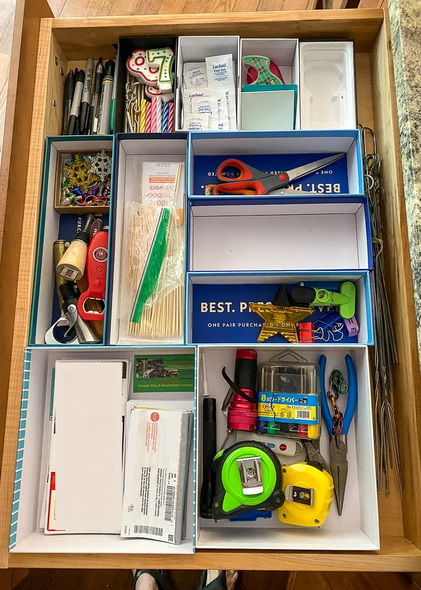 Drawer fitted with reused phone and accessory boxes separating scissors, stationery and household tools