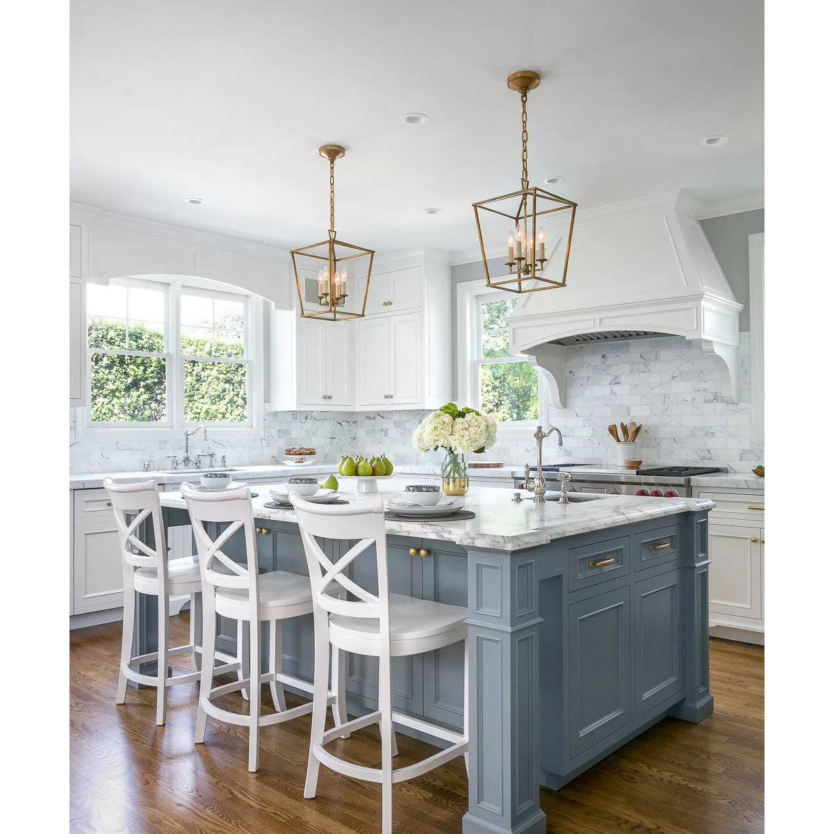 Blue-gray kitchen island with white stools and a small vase beside place settings