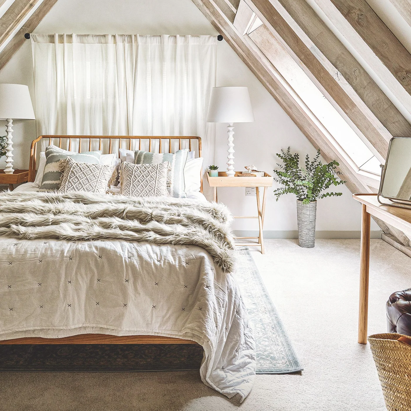 Wooden bed beneath a white gable wall with exposed rafters, roof glazing and pale textured bedding.