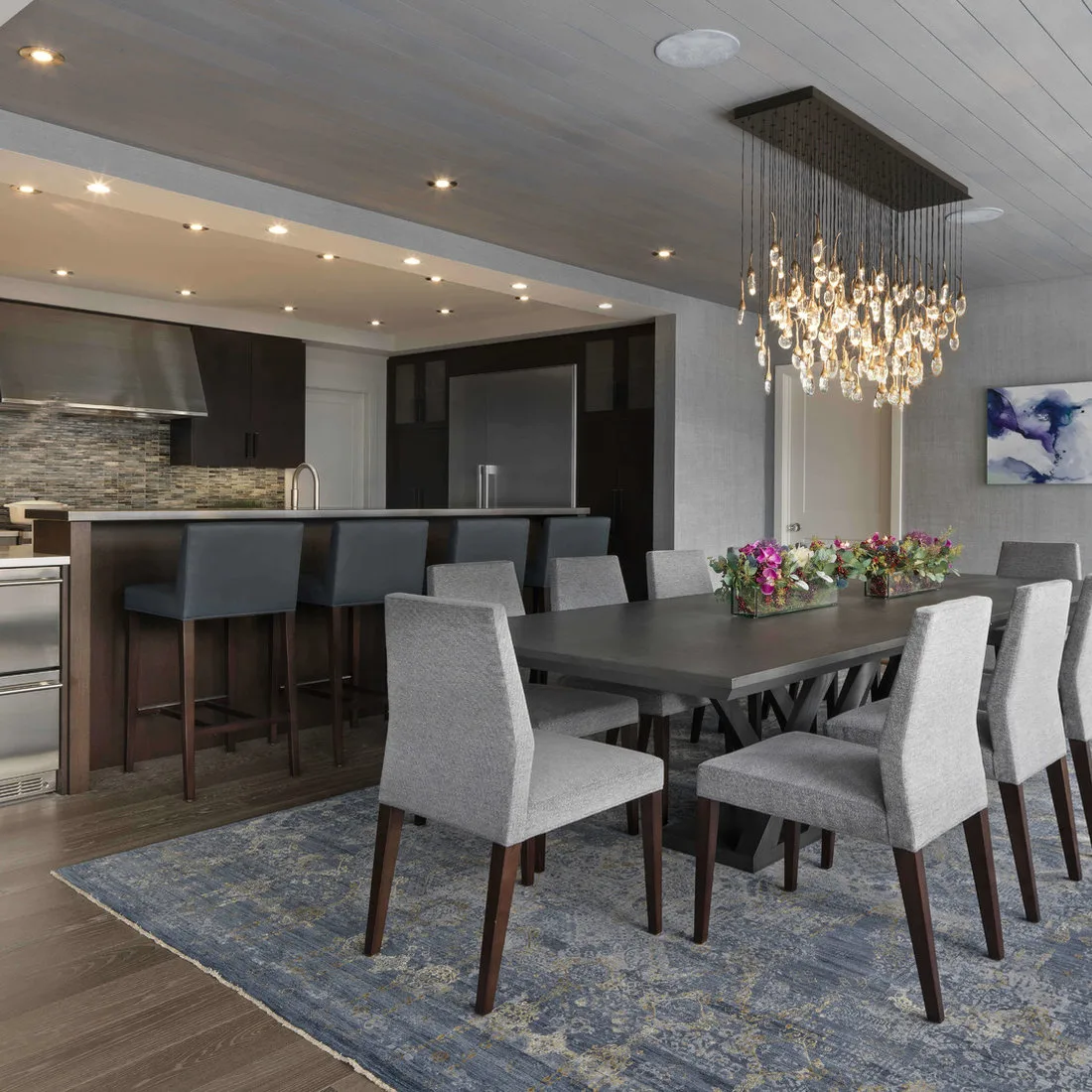 Faded blue patterned rug beneath a dark dining table and gray chairs beside a kitchen island