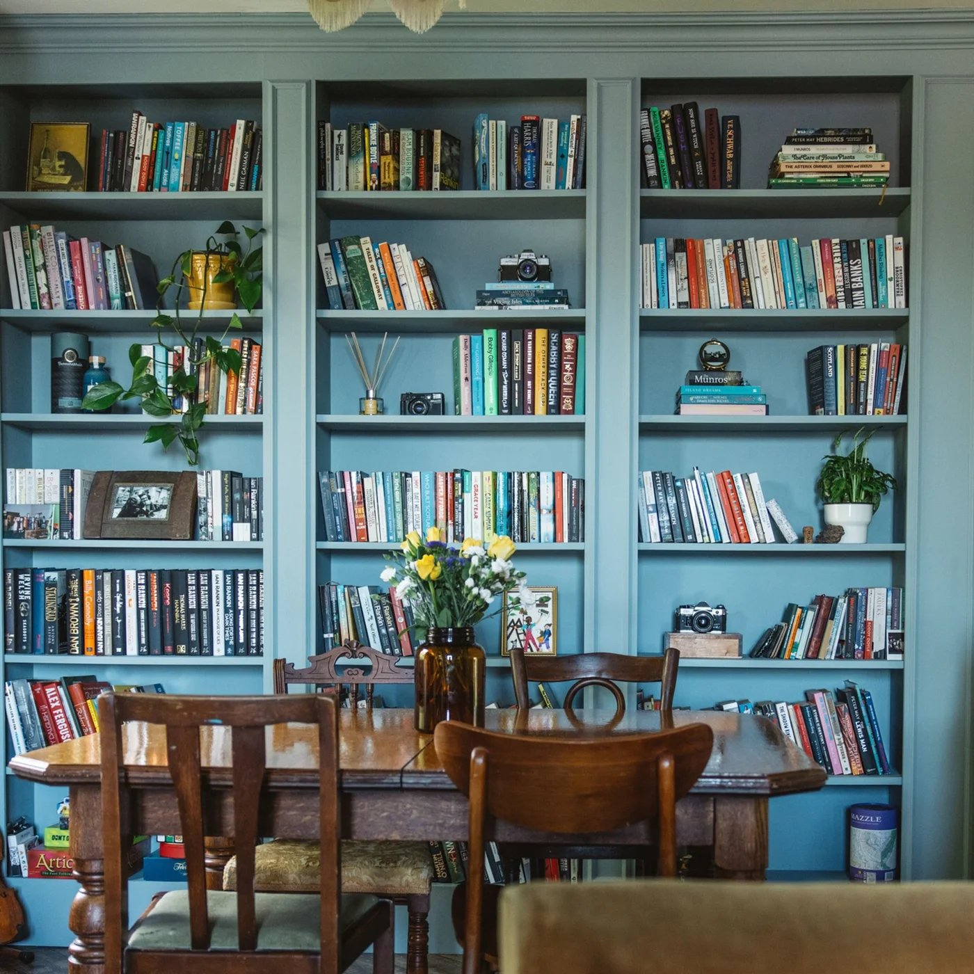 Blue bookcase wall filled with books and small objects behind a wooden dining table