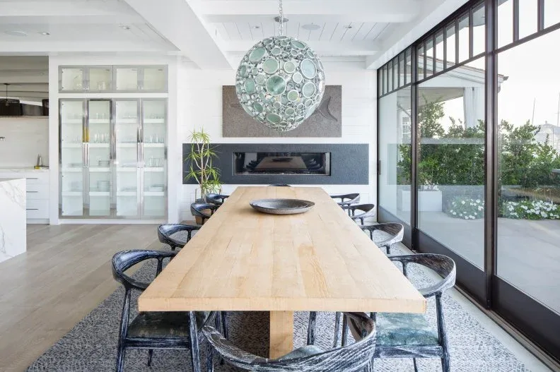 Tall pale glazed dining cabinets beside a horizontal fireplace behind a long wood table and dark chairs