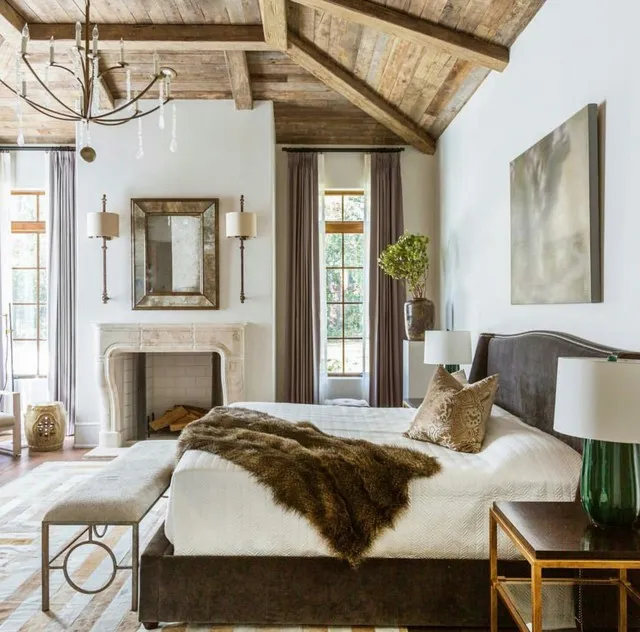 A pale bed sits near a rustic mantel beneath exposed timber rafters.