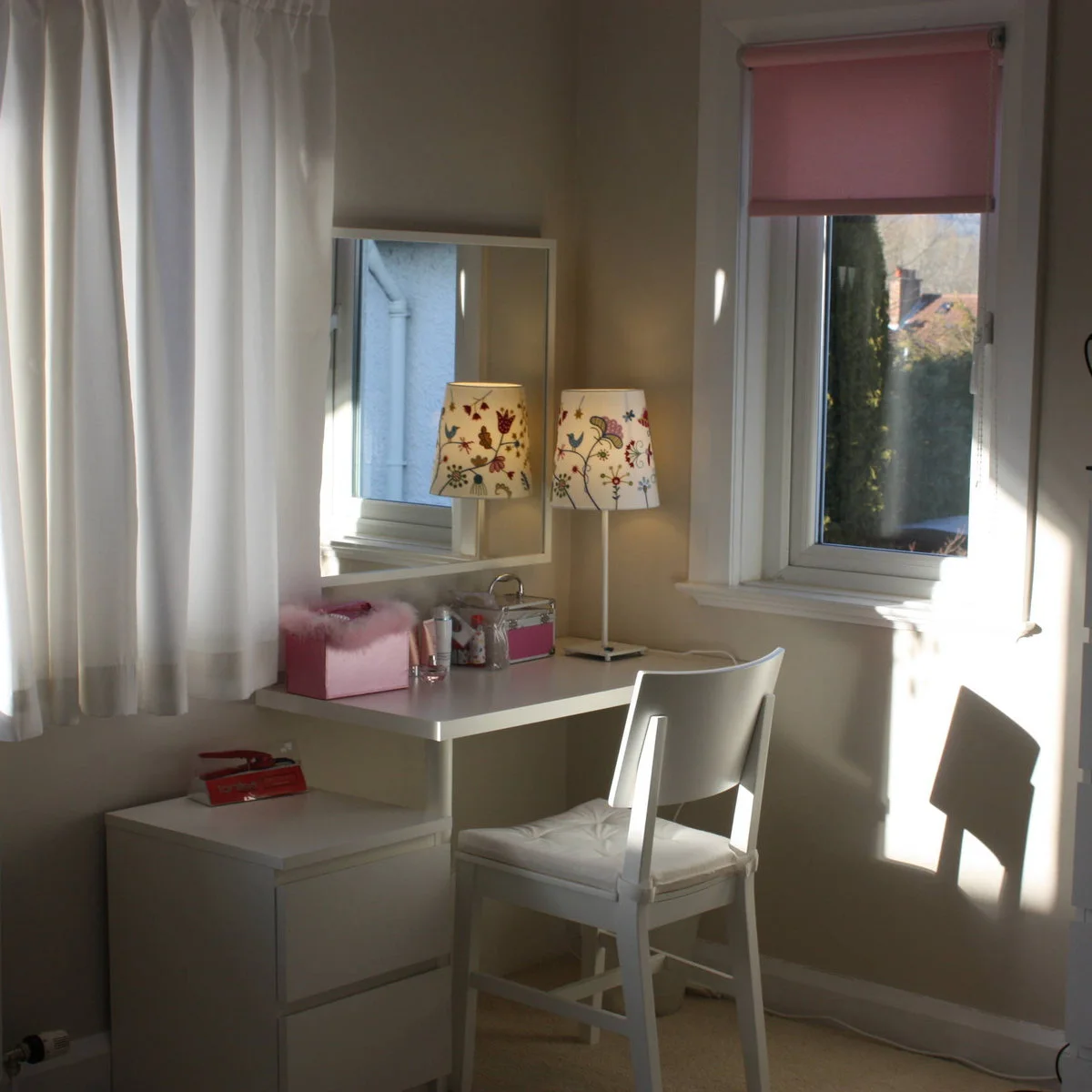 Small teen bedroom dressing desk with a white chair, mirror and patterned lamp beside a window