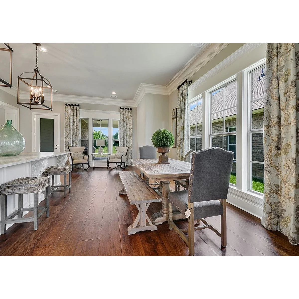 Botanical curtains beside a wood table and bench near a kitchen breakfast counter