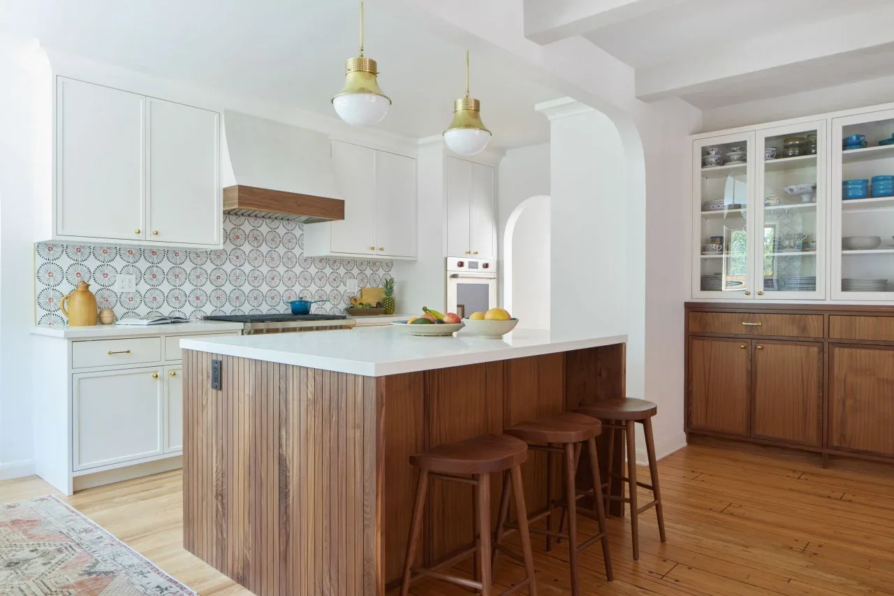 A vertically paneled wood island faces white cabinets, with a wood-based glass-front dresser against the adjoining wall.