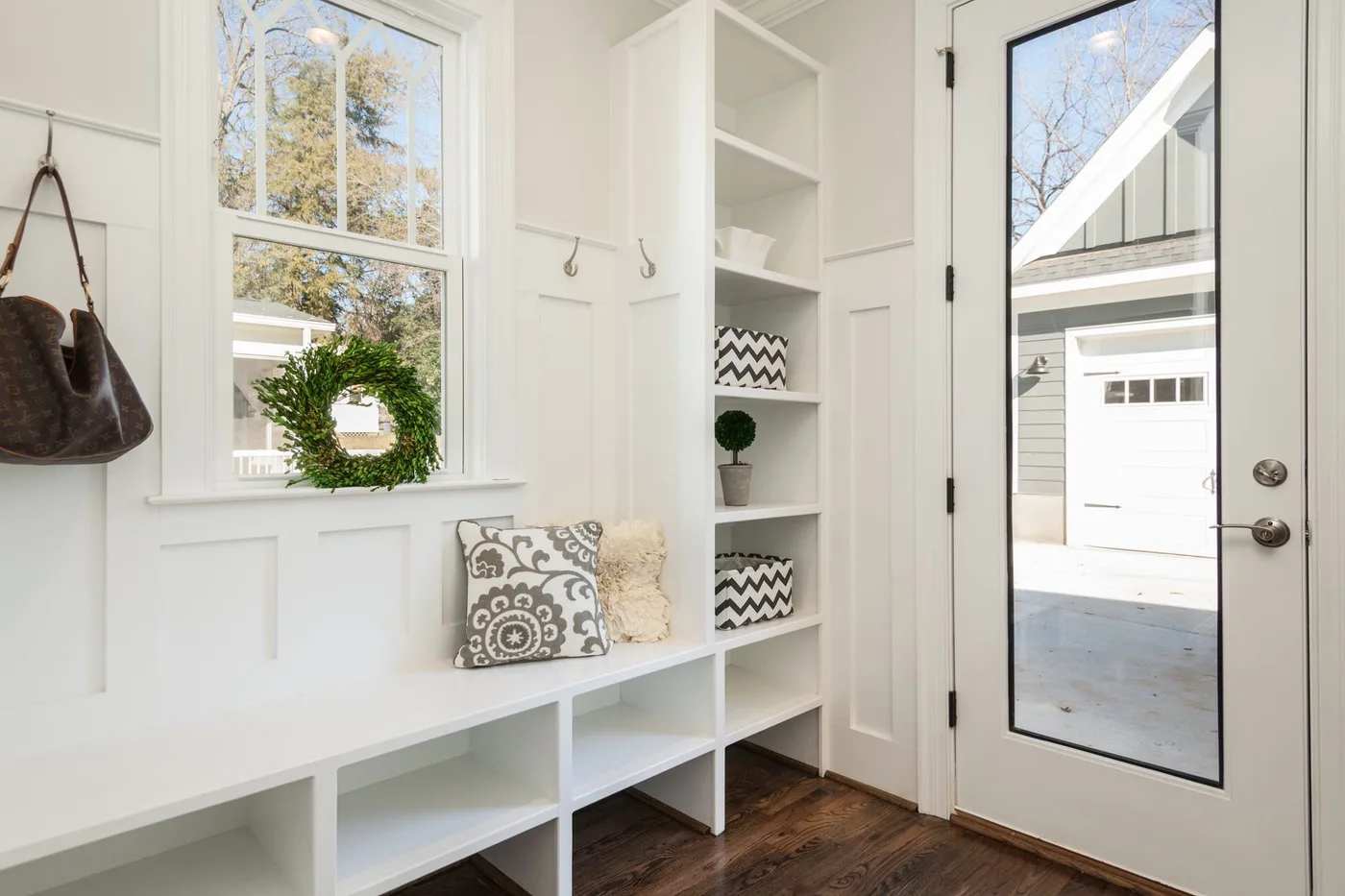 Bright white entry with bench cubbies, a tall open shelf, wall hooks, a window and a glazed door