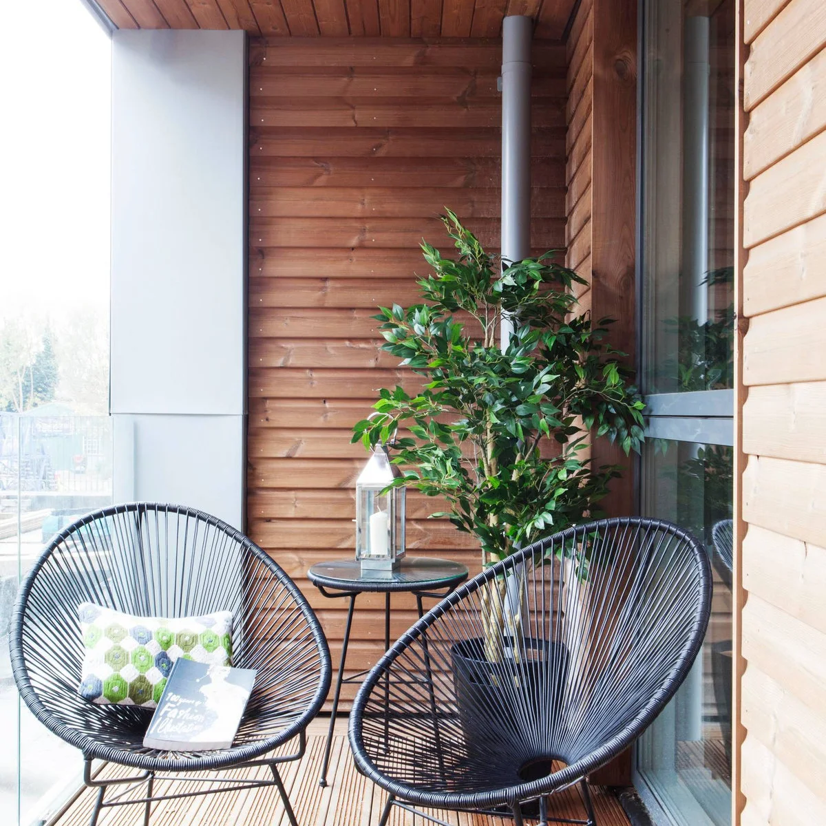 Wood-lined apartment balcony with two black open-framed chairs and a small round table