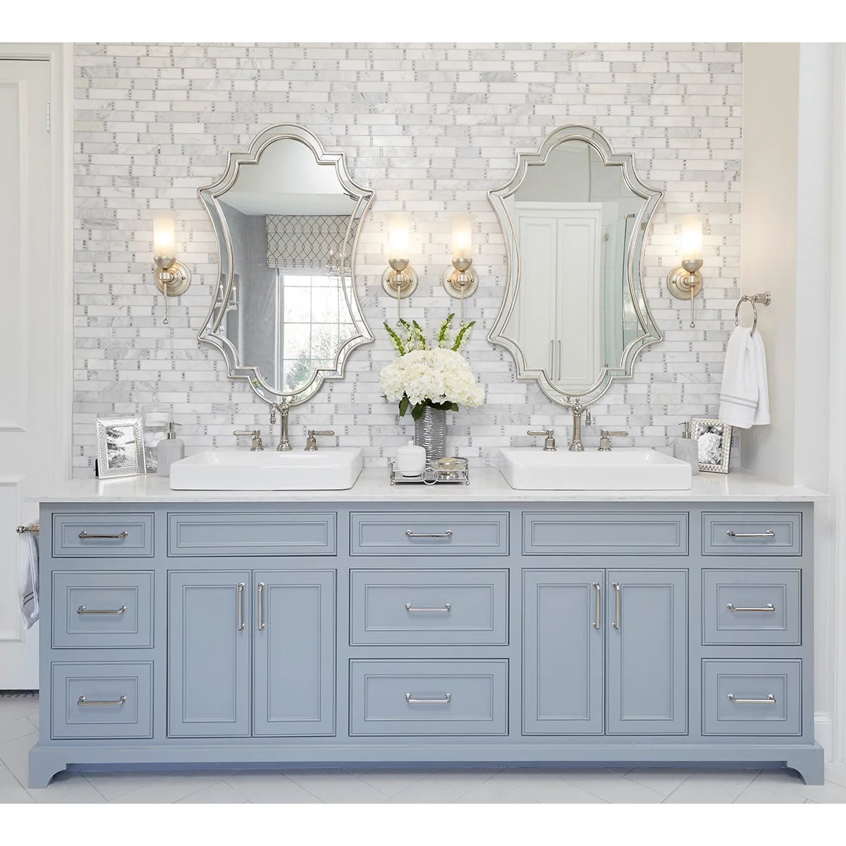 Pale blue double vanity with vessel basins, a central tissue box, small tray and white flowers.
