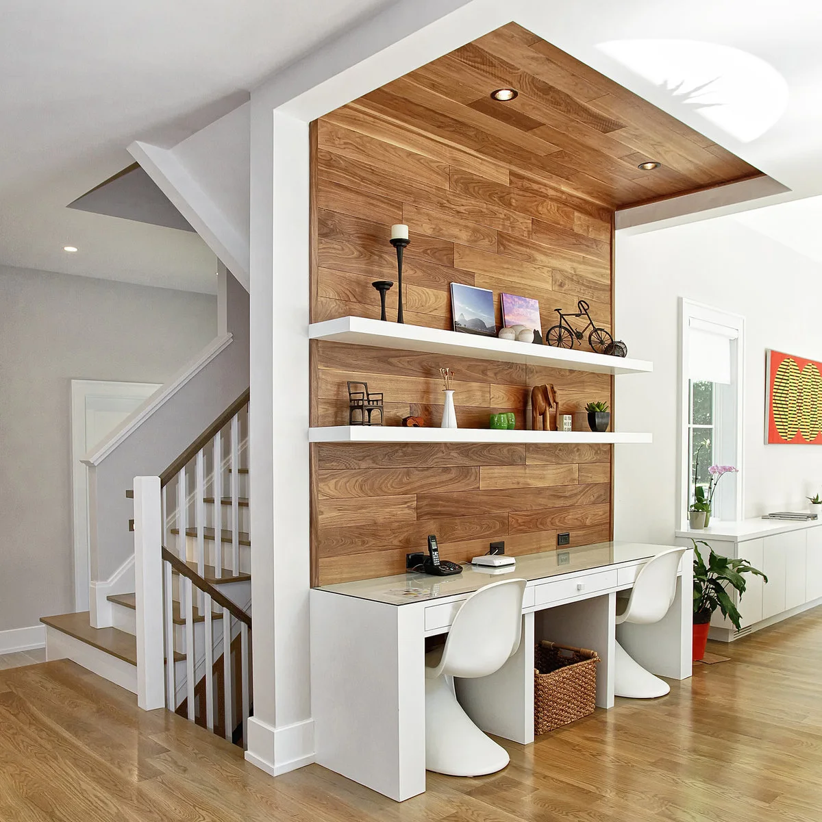 Shared white desk with two chairs beneath a wood-paneled wall and ceiling recess with white shelves